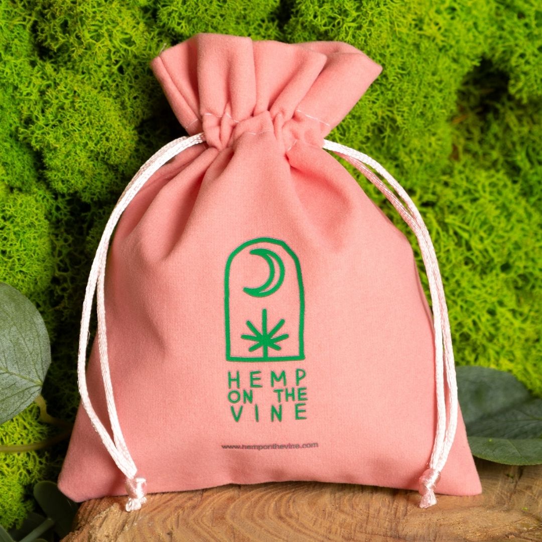 Roze fluwelen zak met groen plantmotief en logo.