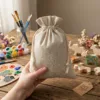 Linnen zakjes in de hand gehouden met knutselmaterialen en creatieve accessoires op de achtergrond